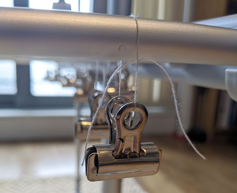 Photograph of a small bulldog clip tied with string, to a rail on a drying rack.  