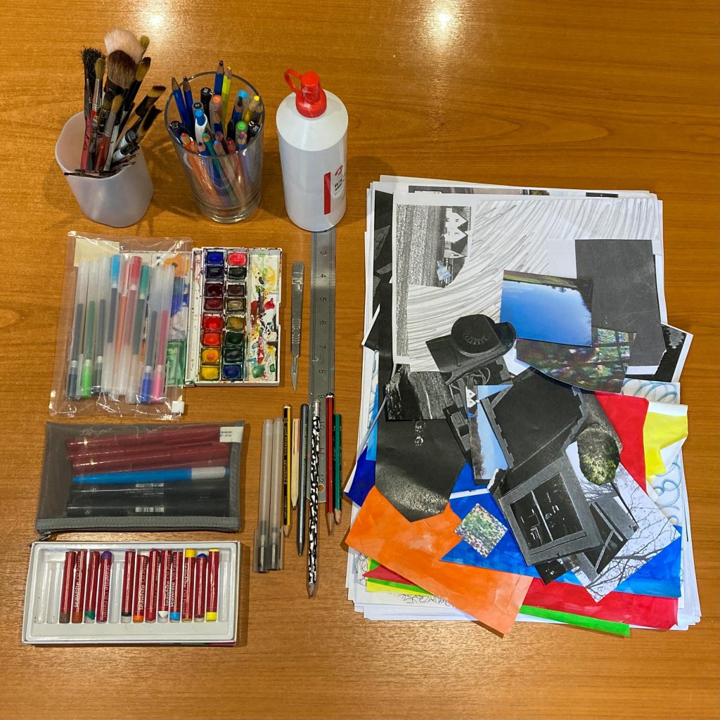 Overview of Izzy's Toolbox. A pot of paintbrushes. A pot of pencils. 2 pencil cases with various pens. A watercolour pallet. A packet of oil pastels. A metal ruler, scalpel and loose pencils. PVA in a bottle. Photographs, coloured paper scraps in a pile. 